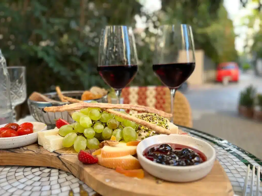 A delicious looking board of appetizers and 2 glasses of wine.