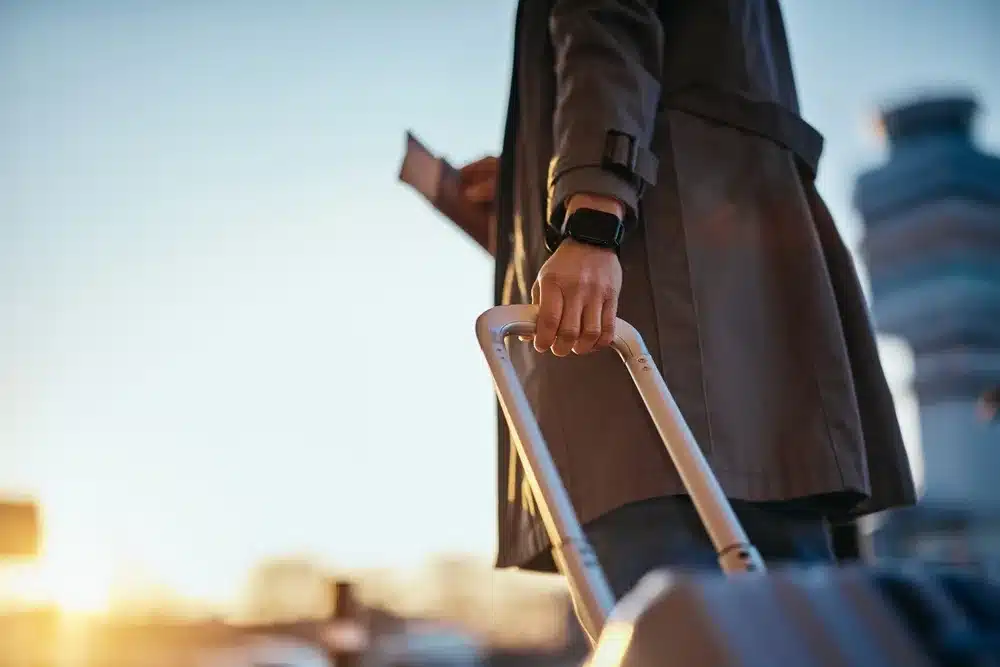 A person pulling their luggage with a passport in the other hand.
