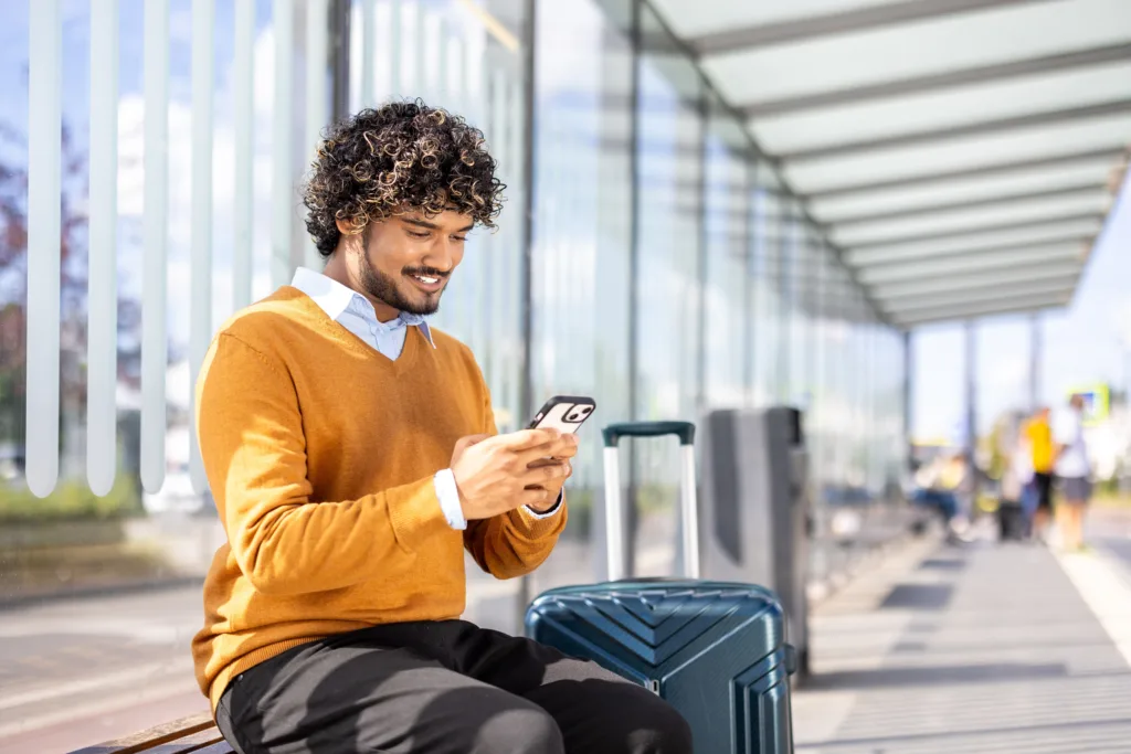 A man sitting at an airport with his luggage, checking his phone.