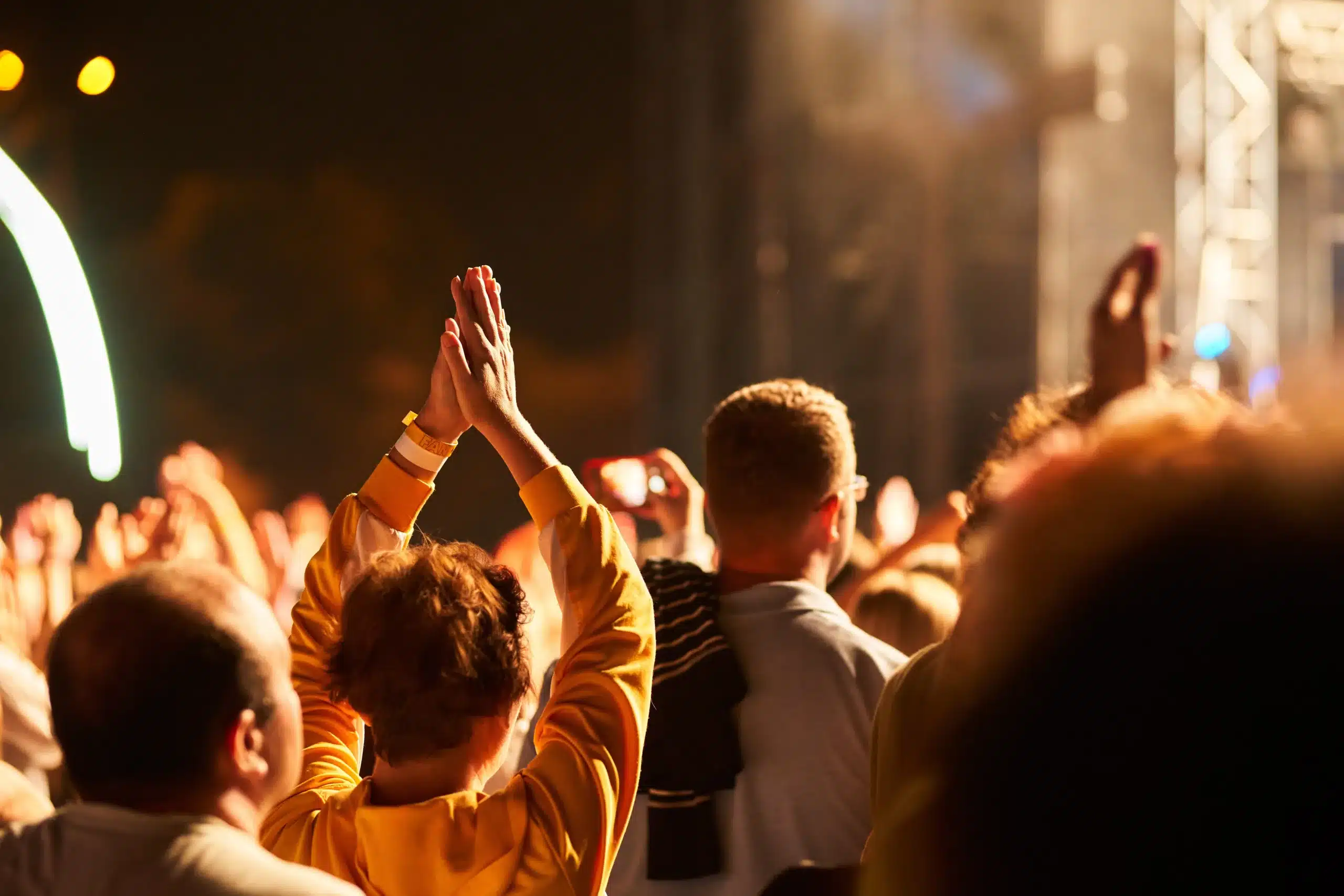 Excited crowd with hands raised at an outdoor music festival at night